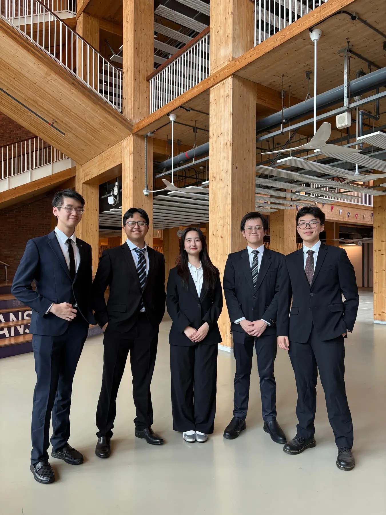 Five people in formal attire standing together inside a timber-framed building.