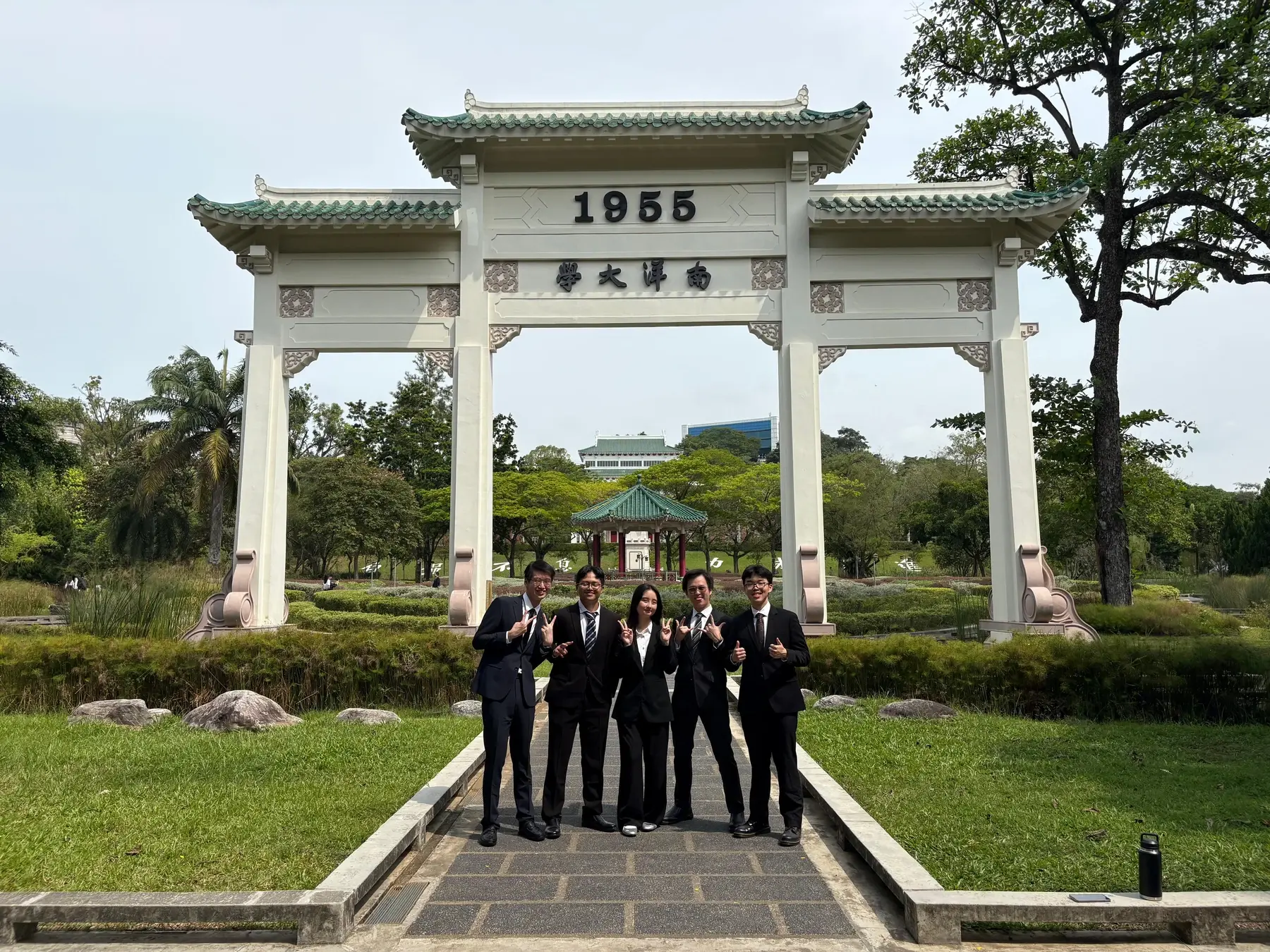 Five people in formal attire standing beneath the Nanyang University arch.