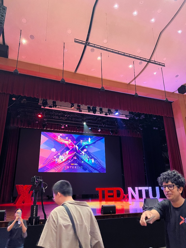 View from the audience floor at Nanyang Auditorium showing attendees and stage production cameras.