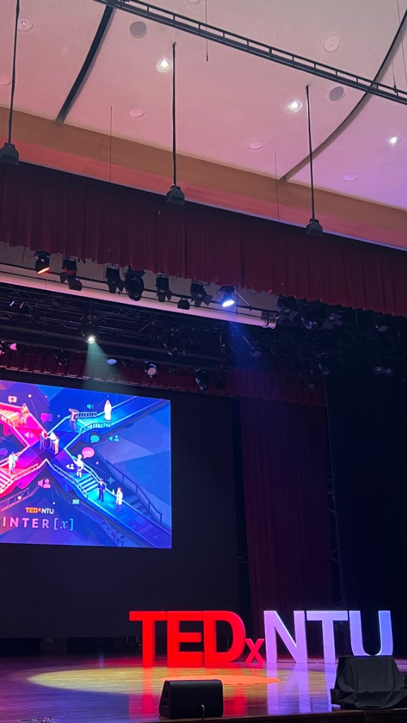 Vertical view of Nanyang Auditorium stage showing illuminated INTER [x] crossroads graphic and TEDxNTU sign.