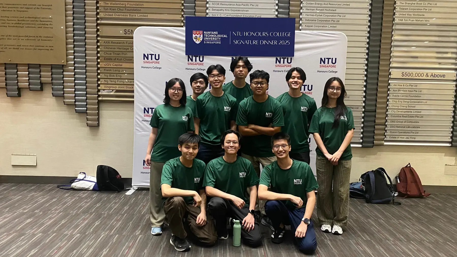 Group wearing green NTU Honours College shirts in front of the Signature Dinner 2025 backdrop.